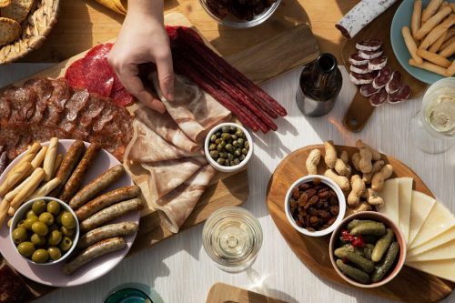 Photographie de plusieurs plateaux apéritifs avec de la charcuterie, du fromage, des arachides, des cornichons, des olives...