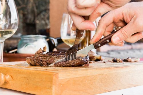Photographie d'une personne en train de découper un steak de boeuf
