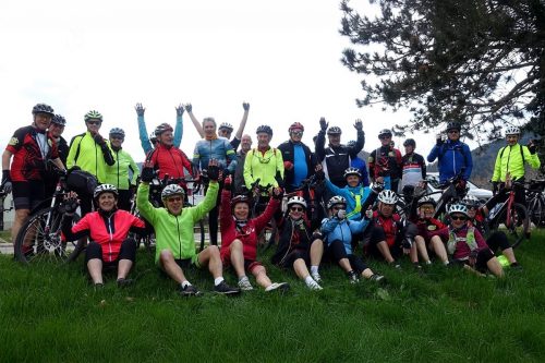 Photographie d'un grand groupe de cycliste à pied ou assis, souriant et levant les bras devant la caméra
