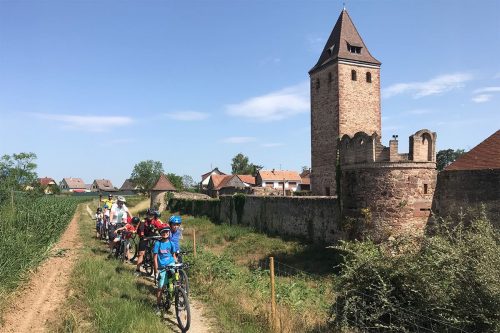 Photographie d'enfant en file indienne à côté des remparts d'une ville médiévale