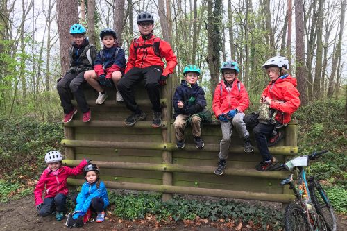 Photographie de plusieurs enfants, casque de vélo sur la tête, assis sur une palissade en forêt
