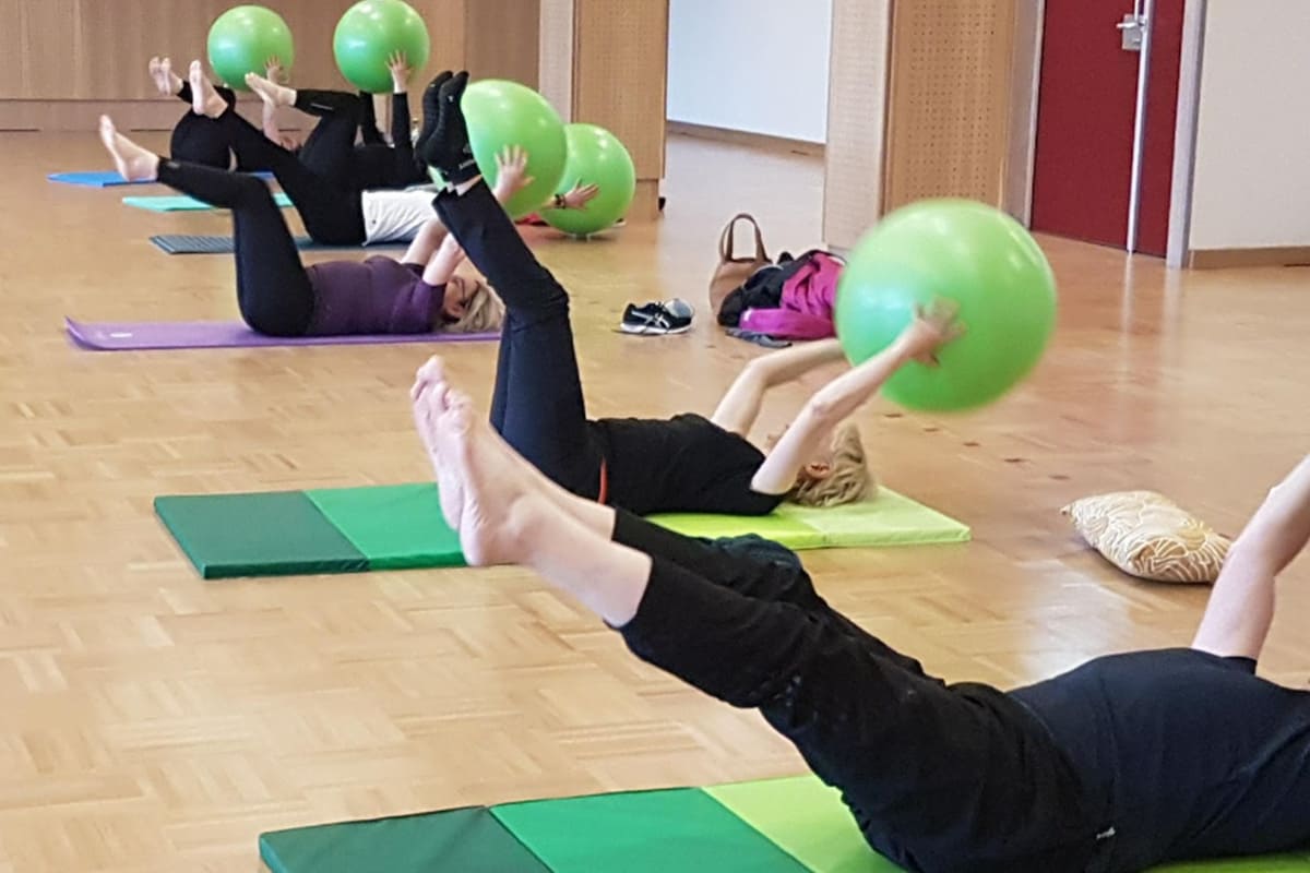 Photographie d'un groupe de l'activité Pilates en intérieur sur des tapis de yoga avec un gros ballon.