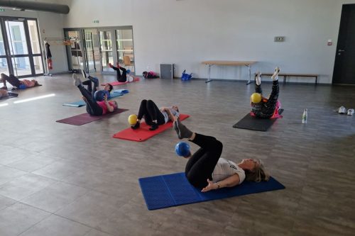 Photographie d'un groupe de l'activité Pilates en intérieur sur des tapis de yoga avec une petite balle en caoutchouc