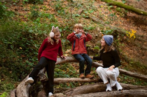 Photographie d'une maman et de ses deux enfants assis sur un arbre en forêt