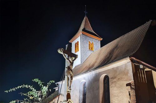 Photographie du clocher d'une église, avec une statue de Jésus crucifié en premier plan.